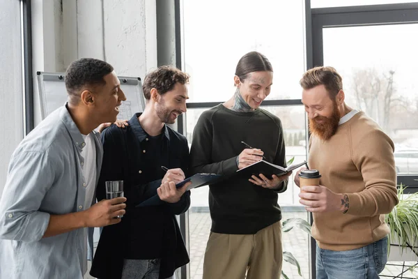 Gente alegre de negocios interracial con cuaderno y portapapeles hablando en la oficina - foto de stock