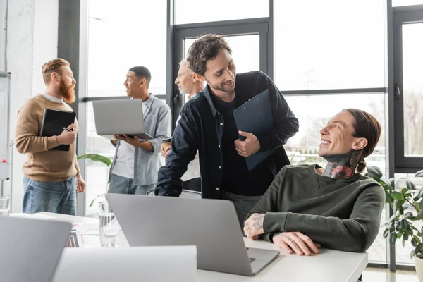 Gente d'affari sorridente con appunti che parla vicino a computer portatile durante riunione in ufficio — Foto stock