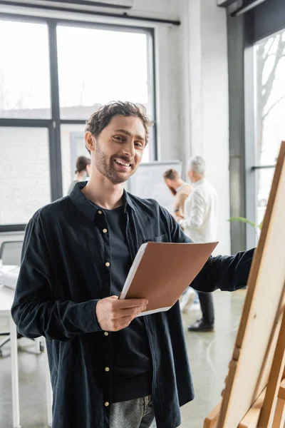 Позитивний бізнесмен тримає паперову теку біля дошки в офісі — стокове фото