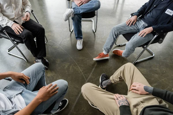 Обрізаний вид міжрасових чоловіків, що сидять на стільцях під час сесії зустрічі алкоголіків в реабілітаційному центрі — стокове фото