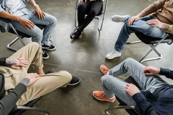 Обрезанный взгляд на межрасовых людей, сидящих на стульях во время встречи алкоголиков в реабилитационном центре — стоковое фото