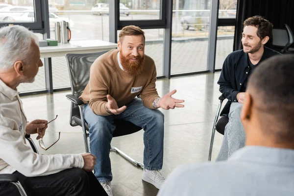 Cheerful man with alcohol addiction talking to interracial group in rehab center — Stock Photo