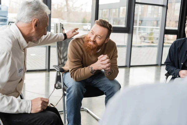 Mature man comforting smiling person with alcohol addiction in rehab center — Stock Photo
