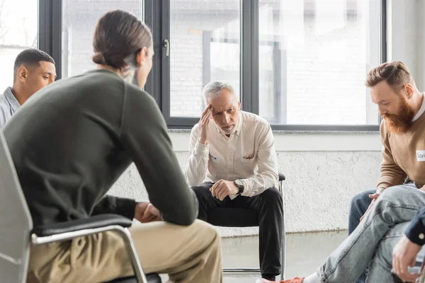 Upset mature man with alcohol addiction sitting in circle during therapy in rehab center — Stock Photo