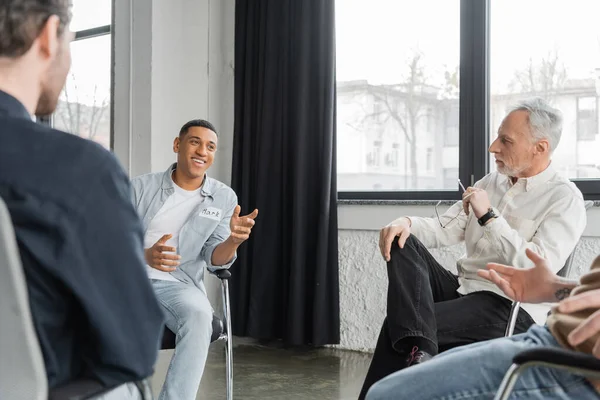 Homme afro-américain joyeux avec dépendance à l'alcool parler pendant la séance de thérapie de groupe dans le centre de réadaptation — Photo de stock