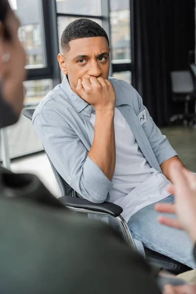 Hombre afroamericano preocupado con adicción al alcohol escuchando la historia durante la terapia en el centro de rehabilitación - foto de stock