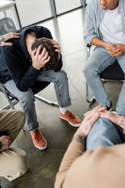 Interracial group calming depressed person with alcohol addiction in rehab center — Stock Photo