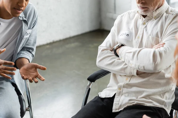 Vista recortada de la persona afroamericana hablando con el hombre durante la reunión de alcohólicos en el centro de rehabilitación - foto de stock