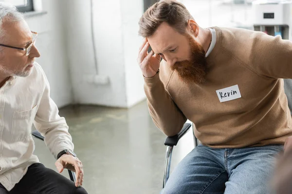 Displeased man with alcohol addiction and name sticker sitting in rehab center — Stock Photo