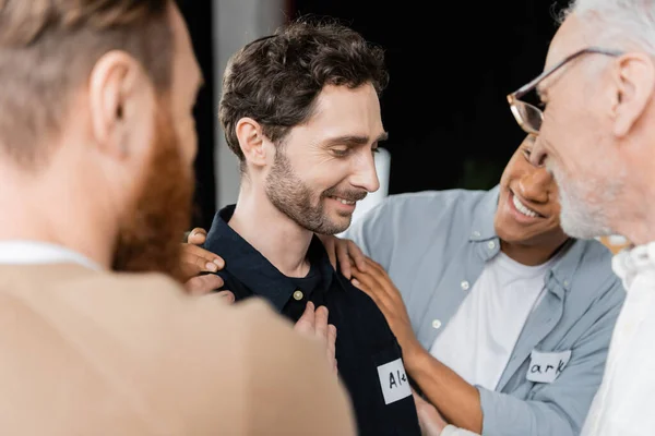 Pessoas multiétnicas positivas abraçando o homem com dependência de álcool no centro de reabilitação — Fotografia de Stock