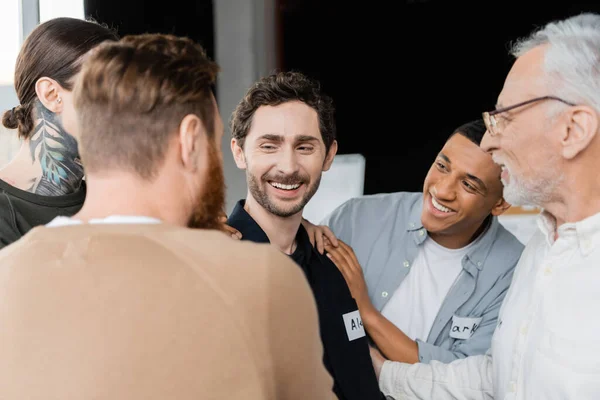 Grupo multiétnico positivo que apoya al hombre sonriente durante la reunión de alcohólicos en el centro de rehabilitación - foto de stock