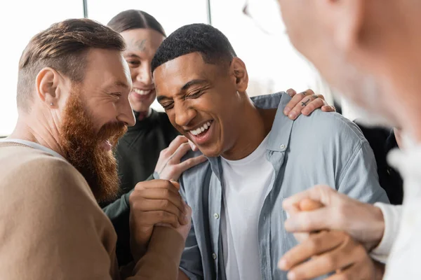 Pessoas positivas abraçando o homem afro-americano durante a reunião de alcoólicos e terapia no centro de reabilitação — Fotografia de Stock