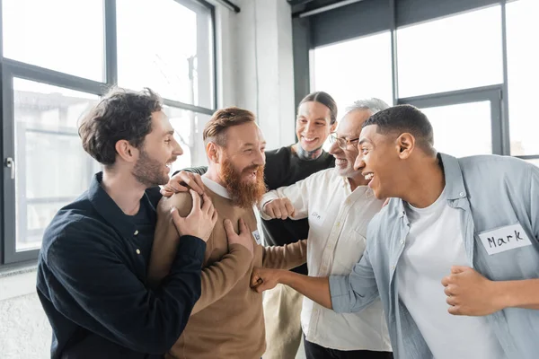 Interracial people hugging cheerful man during alcoholics meeting in rehab center — Stock Photo