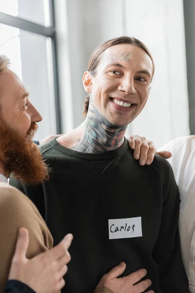 Personas abrazando sonriente hombre tatuado durante la reunión de alcohólicos en el centro de rehabilitación - foto de stock