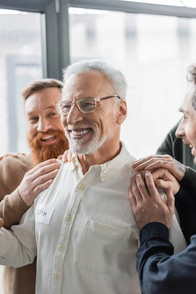 Positive people hugging middle aged man with alcohol addiction during group therapy in rehab center — Stock Photo