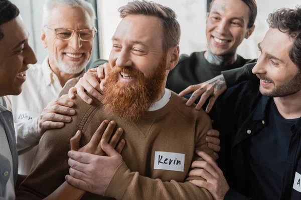 Interracial people hugging smiling man during alcoholics therapy in rehab center — Stock Photo