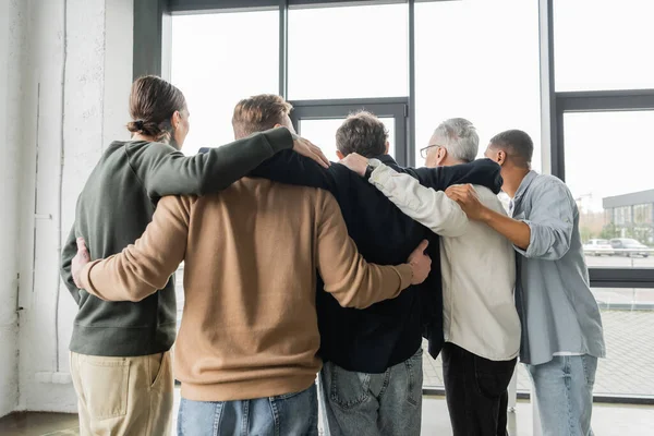Visão traseira de pessoas multiétnicas com dependência de álcool abraçando durante a terapia no centro de reabilitação — Fotografia de Stock