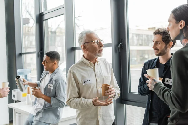 Mature man with alcohol addiction holding paper cup and talking to people in recovery center — Stock Photo