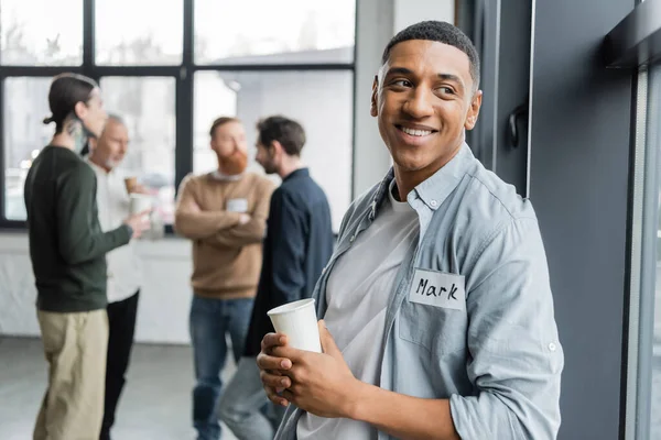 Positive african american man with alcohol addiction holding paper cup in recovery center — Stock Photo