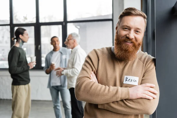 Positive man with name sticker looking at camera during alcoholics meeting in recovery center — Stock Photo