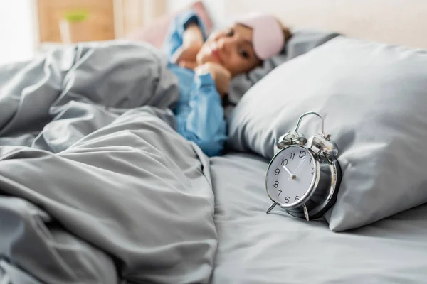 Retro-Wecker auf Bettwäsche neben zufriedener Frau auf verschwommenem Hintergrund — Stockfoto