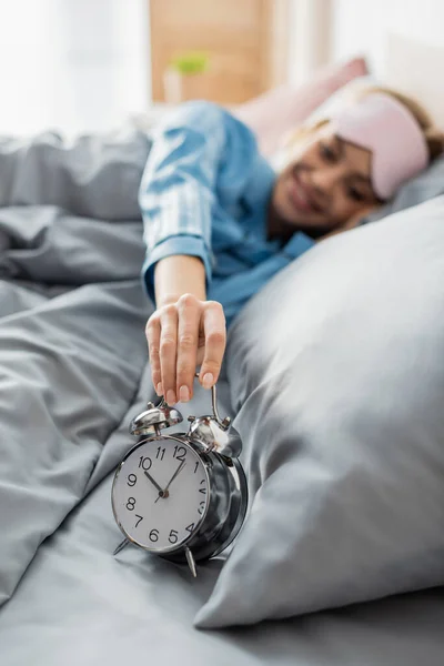 Happy woman taking retro alarm clock while lying on bed in morning — Stock Photo