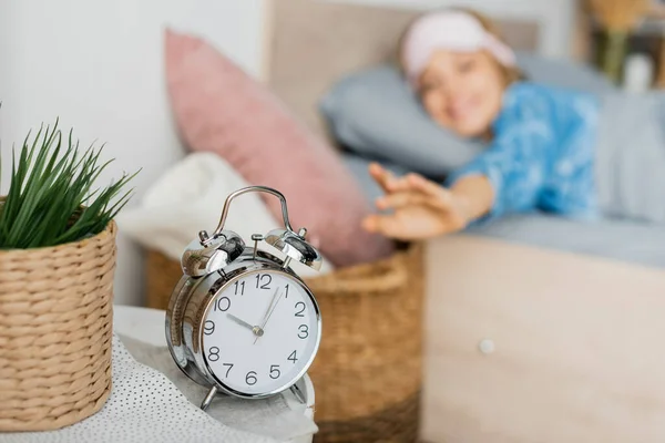 Retro alarm clock on bedside table near happy woman in bed on blurred background — Stock Photo