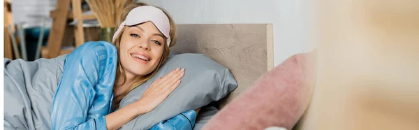 Весела жінка в сплячій масці і блакитна піжама лежить в ліжку, банер — стокове фото
