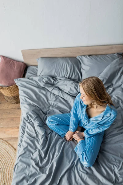 Vue du dessus des pieds nus et femme joyeuse en pyjama bleu assis sur le lit — Photo de stock