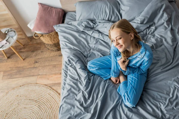 Вид зверху на позитивну жінку в блакитній піжамі, підморгуючи в спальні — стокове фото