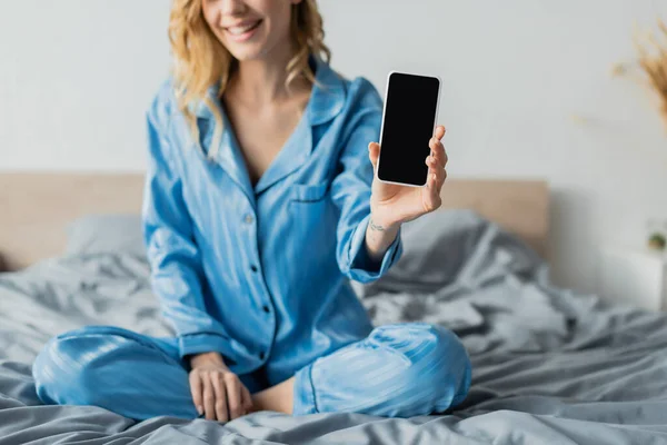 Vue recadrée de femme heureuse en pyjama bleu tenant smartphone avec écran blanc — Photo de stock