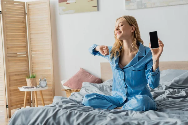 Femme heureuse en pyjama bleu tenant smartphone avec écran blanc — Photo de stock