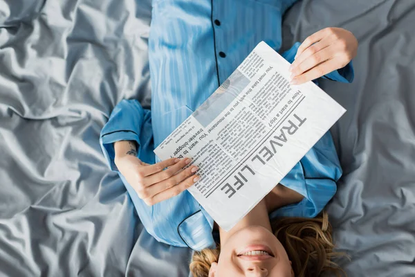 Top view of cropped woman smiling while reading travel life newspaper in bed — Stock Photo