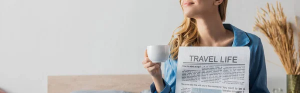 Обрезанный вид на довольную молодую женщину проведение путешествия жизнь газеты и чашку кофе в спальне, баннер — стоковое фото