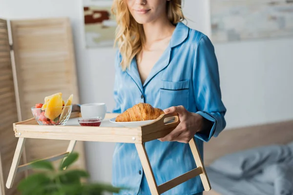 Vista ritagliata di donna soddisfatta in pigiama blu vassoio con prima colazione in camera da letto — Foto stock