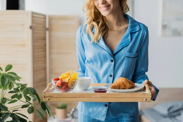 Vista ritagliata della donna felice nel vassoio blu della tenuta di biancheria da notte con la prima colazione in camera da letto — Foto stock