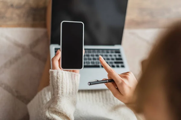 Visão parcial do freelancer borrado apontando com o dedo para o smartphone com tela em branco perto do laptop — Fotografia de Stock