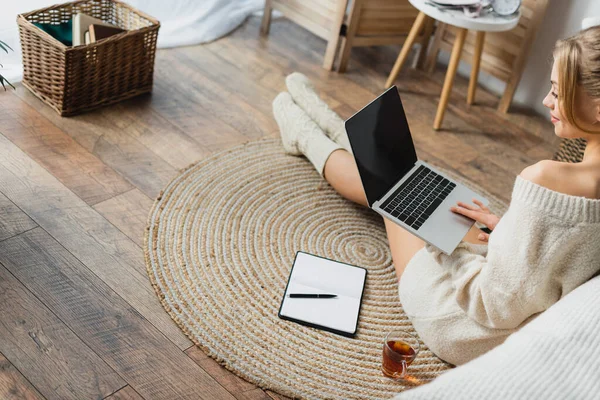 Блондинка в свитере и вязаных носках с помощью ноутбука в современной квартире — стоковое фото