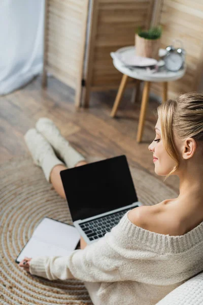 Чарівна жінка в светрі і шкарпетках, використовуючи ноутбук в сучасній квартирі — стокове фото