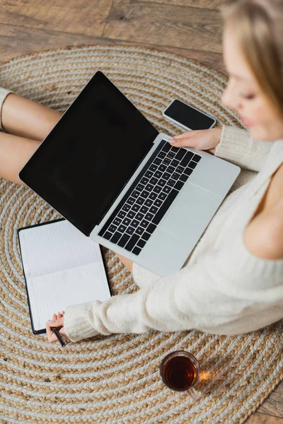 Vista superior da mulher desfocada em suéter usando laptop e tomar notas no notebook — Fotografia de Stock