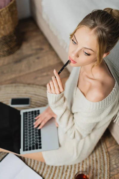 Vista aérea da mulher pensativa em suéter sentado com laptop no apartamento moderno — Fotografia de Stock