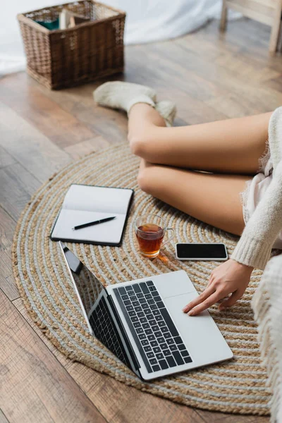 Vista cortada de mulher jovem sentado perto de dispositivos e xícara de chá enquanto trabalhava em casa — Fotografia de Stock
