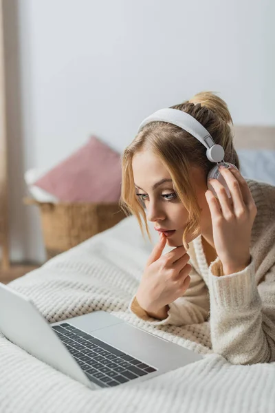 Focused woman in wireless headphones watching movie on laptop in bedroom — Stock Photo