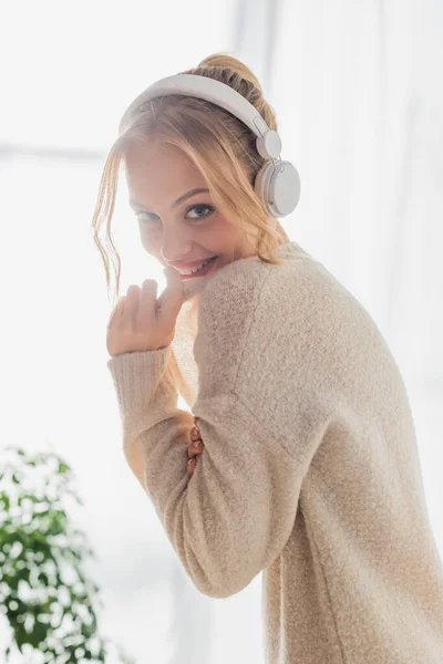 Alegre joven mujer escuchando música en auriculares inalámbricos mientras se divierten en casa - foto de stock