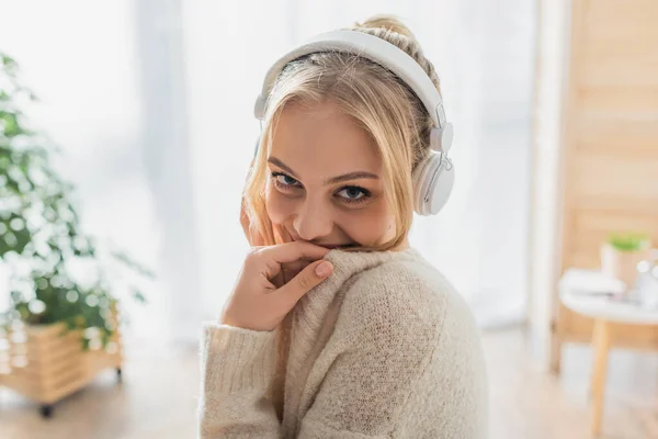 Mujer despreocupada escuchando música en auriculares inalámbricos mientras mira a la cámara - foto de stock