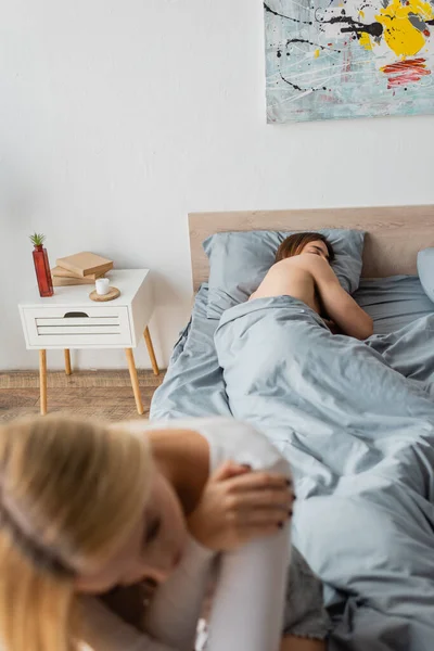 Hombre sin camisa durmiendo debajo de la manta después de una noche con la mujer rubia en primer plano borrosa - foto de stock