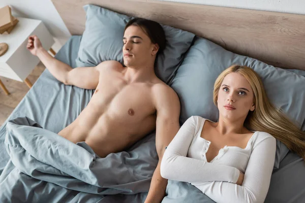 Vista ad alto angolo di donna imbarazzata svegliarsi con uomo senza camicia dopo una notte stand — Foto stock