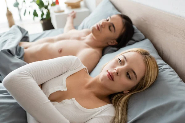 Мужчина без рубашки спит под одеялом рядом с запутавшейся блондинкой после одной ночи — стоковое фото
