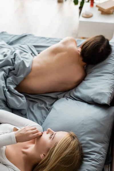 Vue grand angle de la femme embarrassée couvrant la bouche tout en regardant homme torse nu dans son lit après une nuit stand — Photo de stock