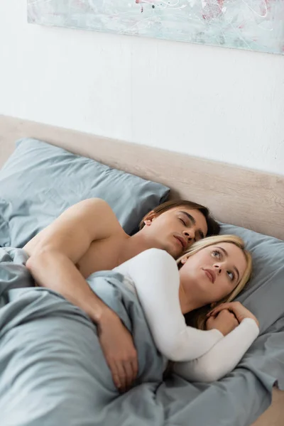 Mujer confundida acostada en la cama con el hombre dormido después de una noche de aventura - foto de stock